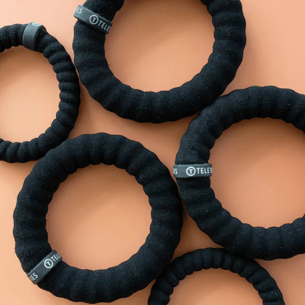 Black hair ties with visible brand label on a beige background