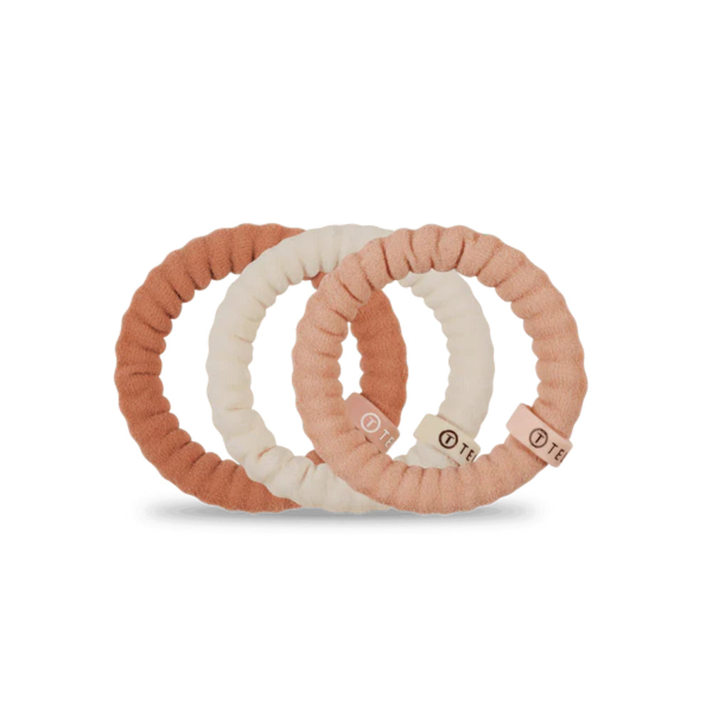 Three scrunchies in peach, white, and pink on a white background