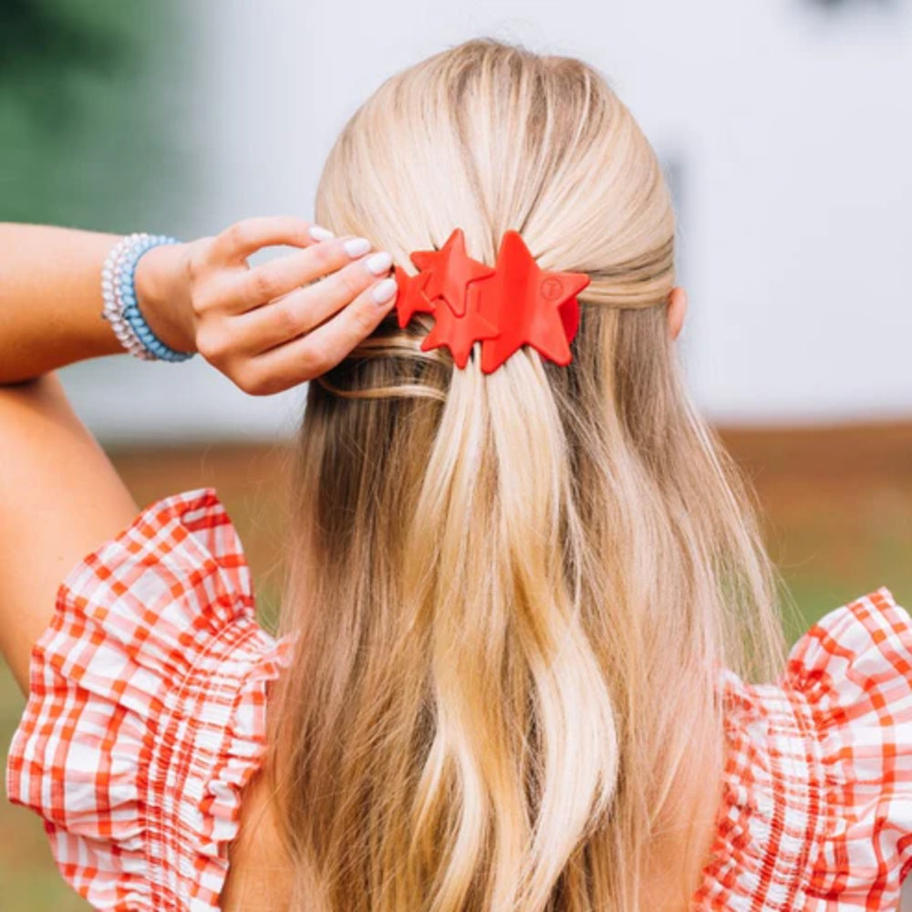 Person with blonde hair wearing a red hair clip, wearing a red and white checkered shirt.
