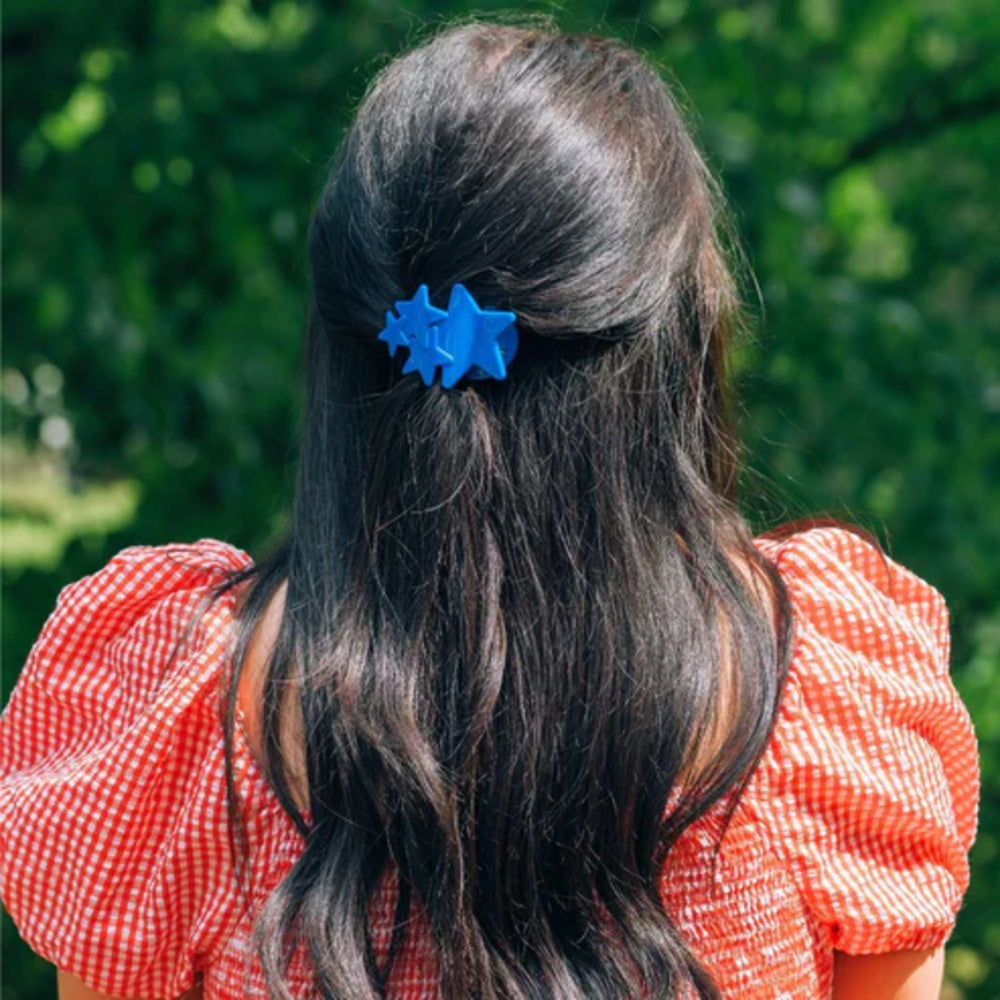 Person with long dark hair wearing a blue hair clip, standing against a blurred green background