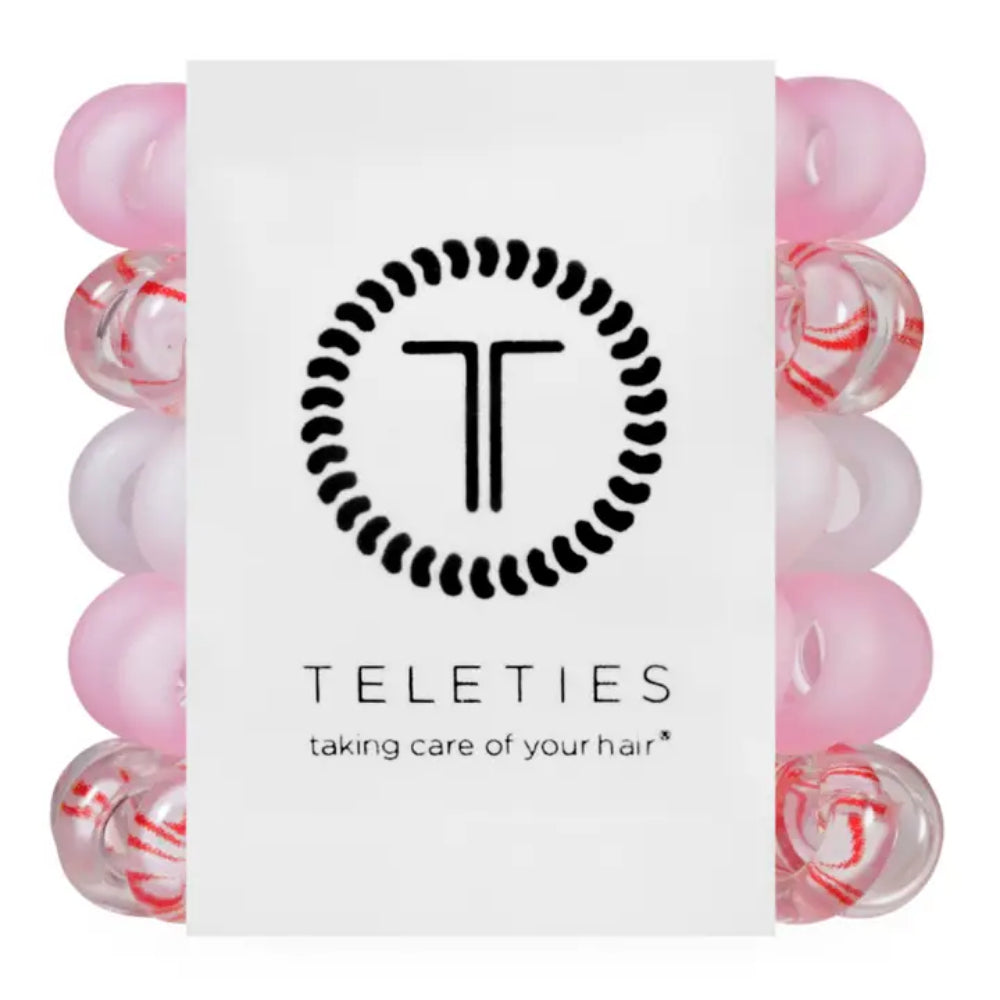 A white rectangular product card centered in front of a set of pink and translucent hair care beads. The card displays the black circular 'T' logo and the brand name 'TELETIES' with the tagline 'taking care of your hair'.