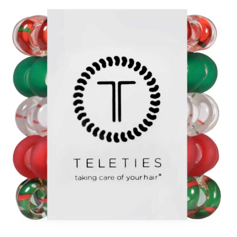 A white rectangular product card centered on a white background, flanked by two vertical rows of round hair care beads in red, green, and clear. The card displays the black logo and text 'TELETIES' with the tagline 'taking care of your hair'.