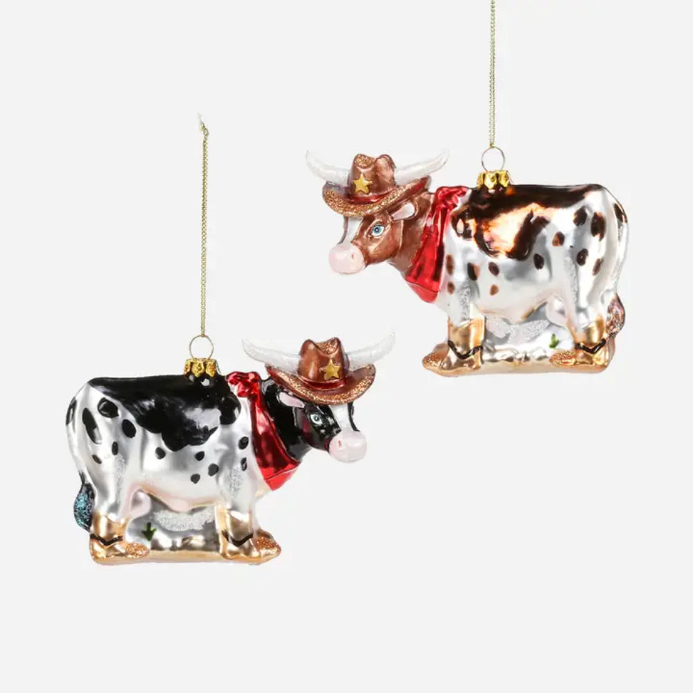 Two decorative hanging cow ornaments on a plain light gray background. One cow is black and white with brown spots, and the other is white and brown with black spots; both wear brown cowboy hats and red neck ribbons.