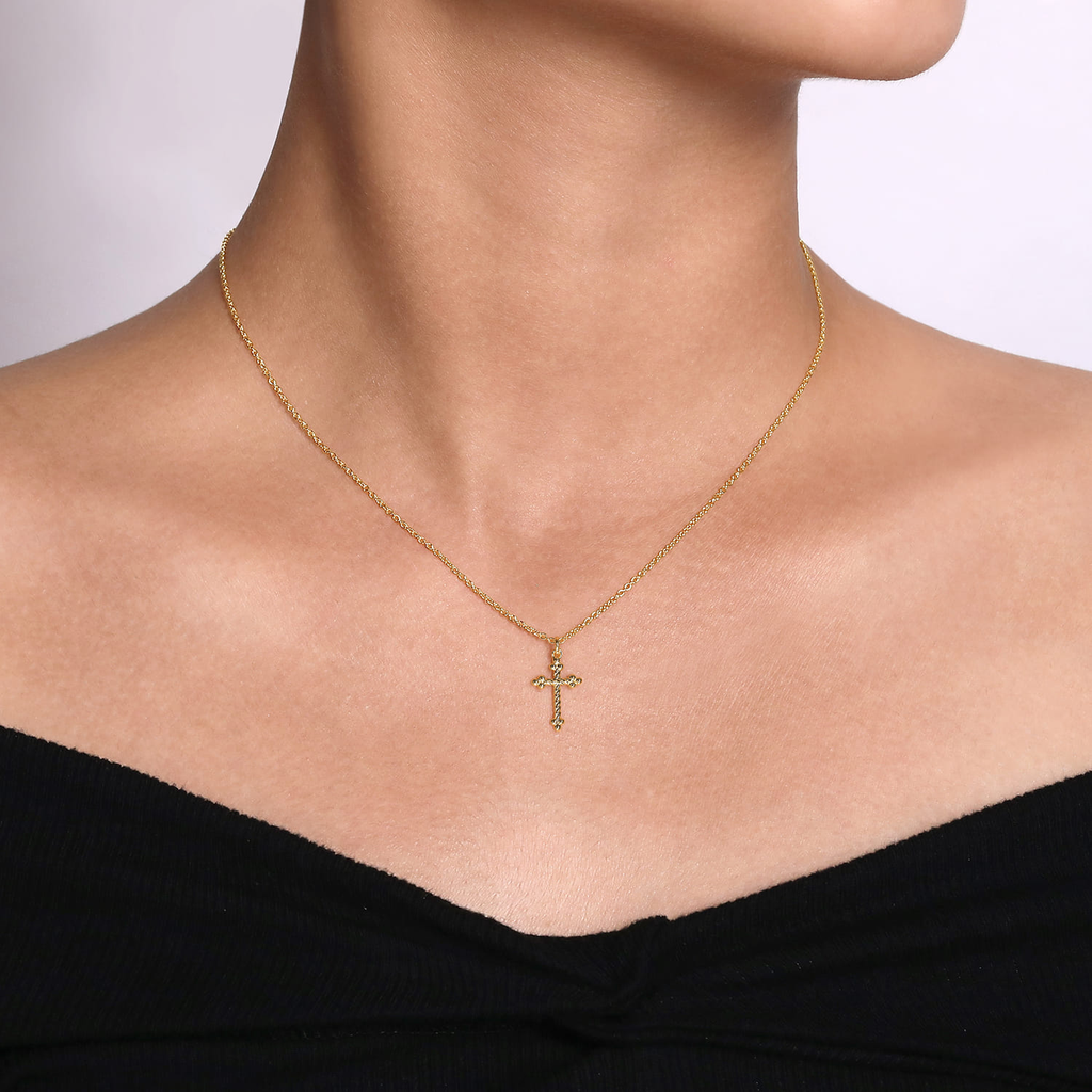 Gold necklace with a cross pendant on a person wearing a black top.