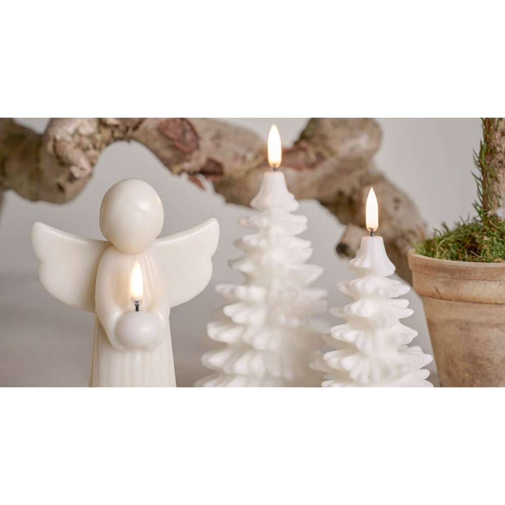 White Christmas-themed candle set featuring an angel figurine holding a small glowing candle, two tree-shaped candles, and a potted plant in the background.