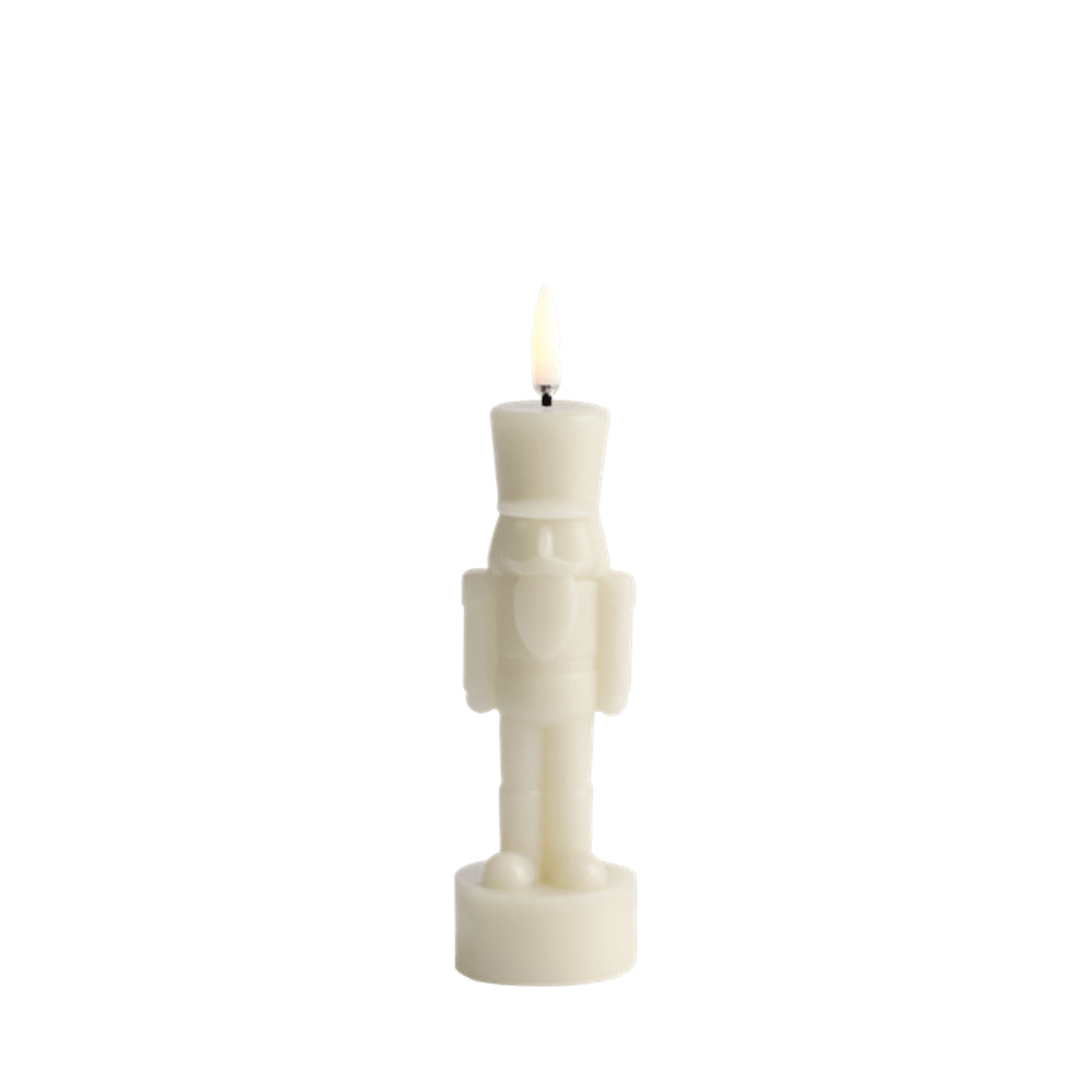 An off-white nutcracker-shaped candle with a lit flame, centered on a solid white background.