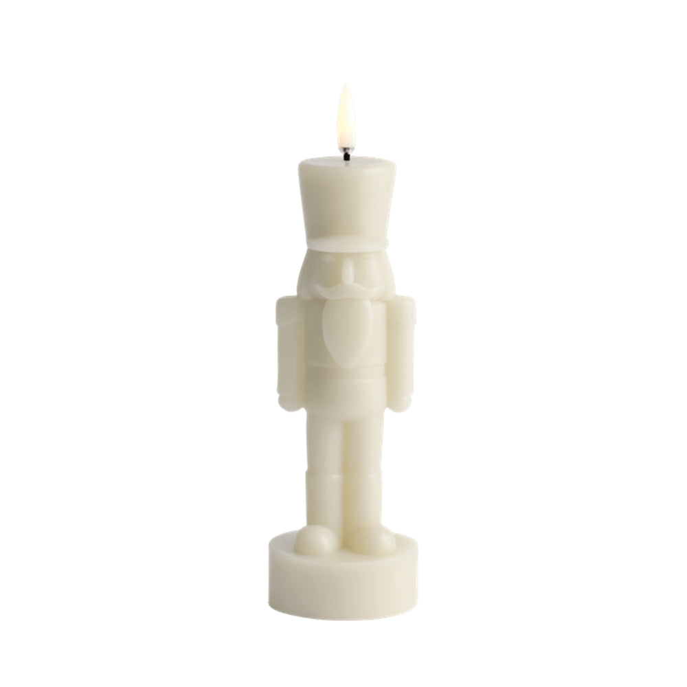 An off-white nutcracker-shaped candle with a lit flame, shown against a solid white background.