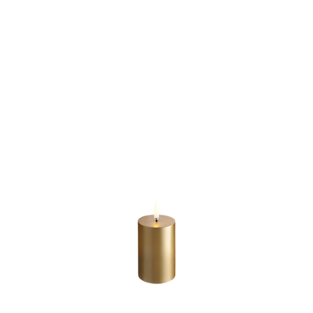 A single lit gold pillar candle with a small flame, centered against a solid white background.