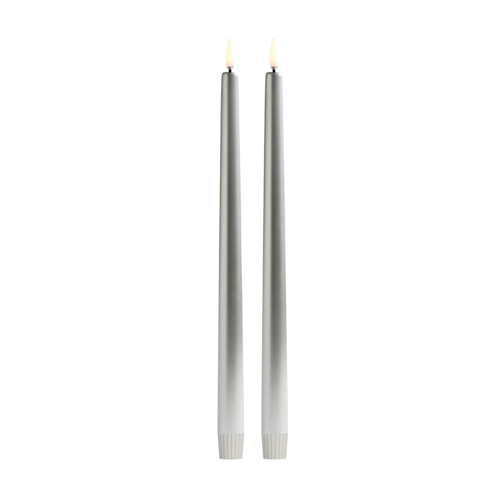 Two tall, slender silver taper candles with lit flames, standing upright against a solid white background.