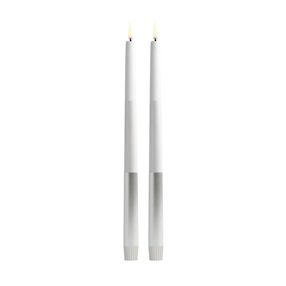 Two slim white taper candles with silver-toned bases and small flame tips, shown upright on a plain white background.