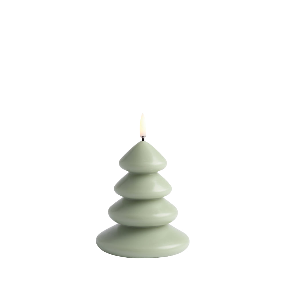 A lit Christmas tree-shaped candle in a muted sage green color, shown against a solid white background.