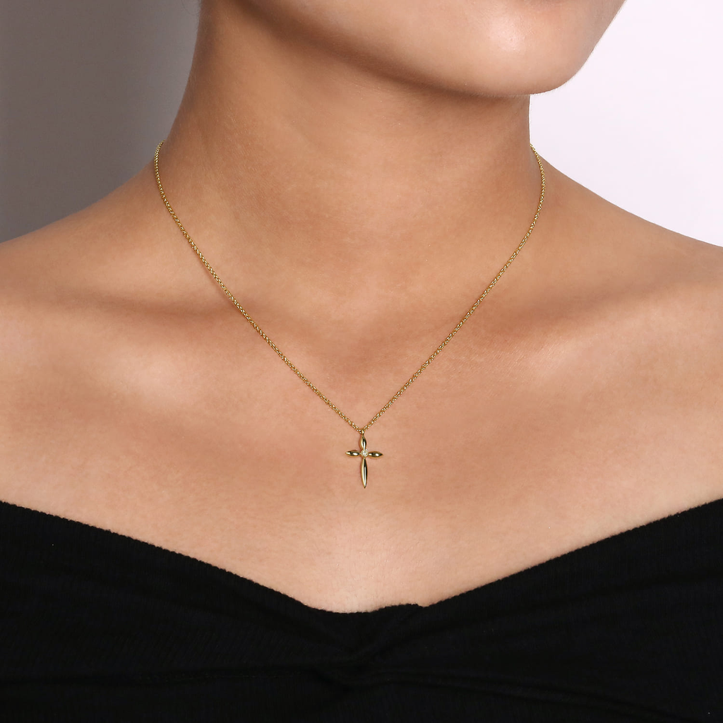 Gold necklace with a cross pendant on a person wearing a black top against a neutral background