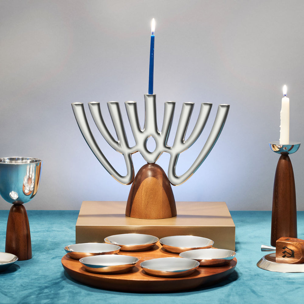 Modern menorah with wooden base and metal branches on a blue tablecloth.