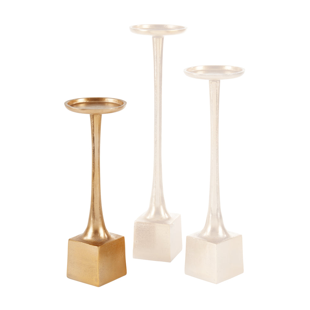 Three metallic candle holders with square bases, displayed on a clean white background. The set includes one gold holder and two silver holders of varying heights.