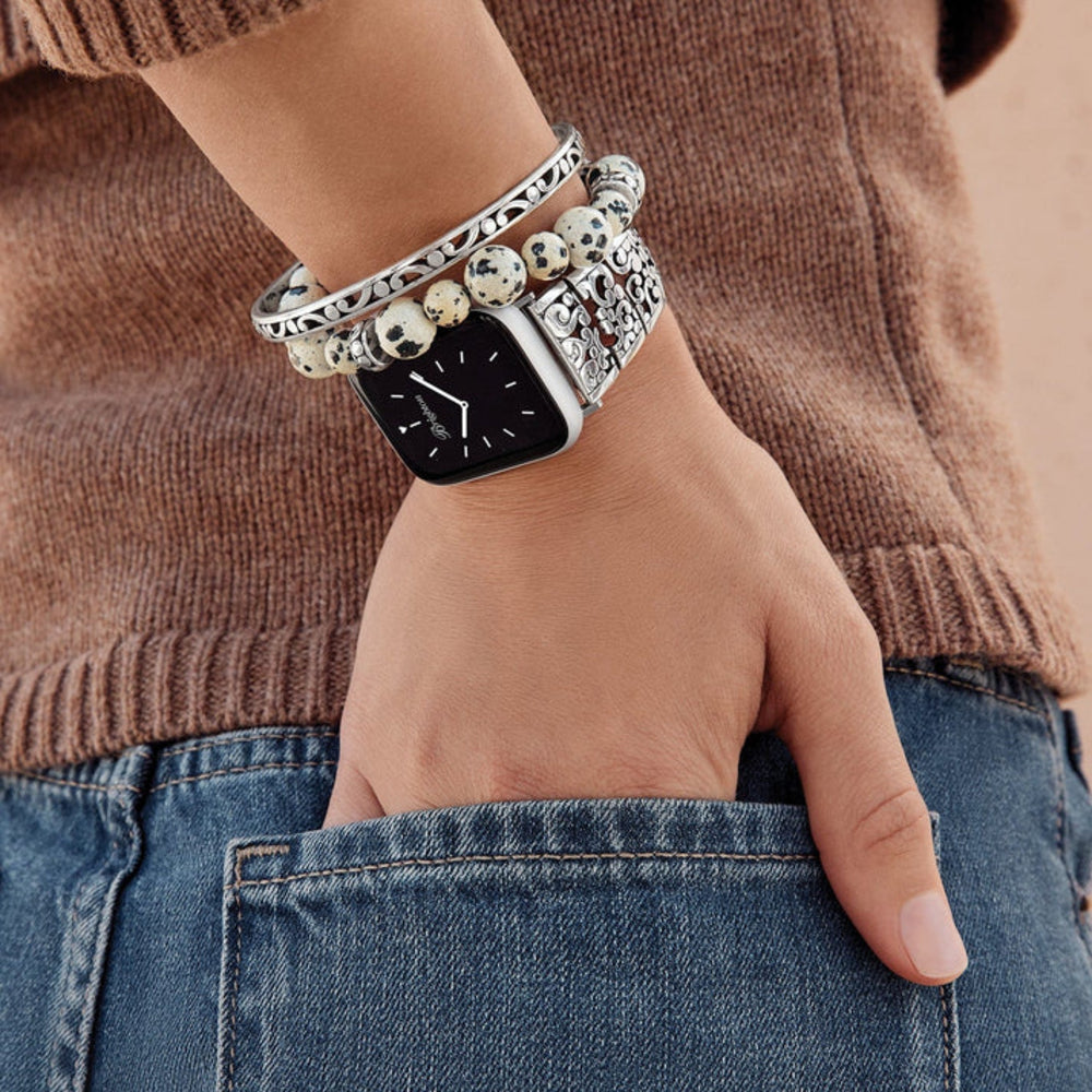 Hand wearing a smartwatch with multiple bracelets, against a brown sweater and blue jeans background.