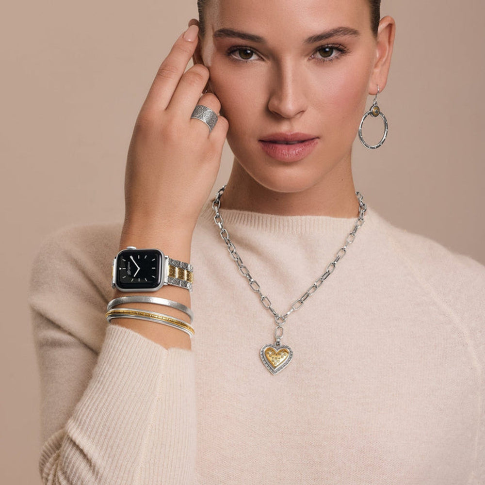 Woman wearing a collection of silver jewelry including a watch, necklace, and earrings on a beige background.