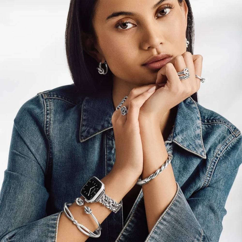 Woman wearing silver jewelry including a watch, bracelets, and rings on a white background
