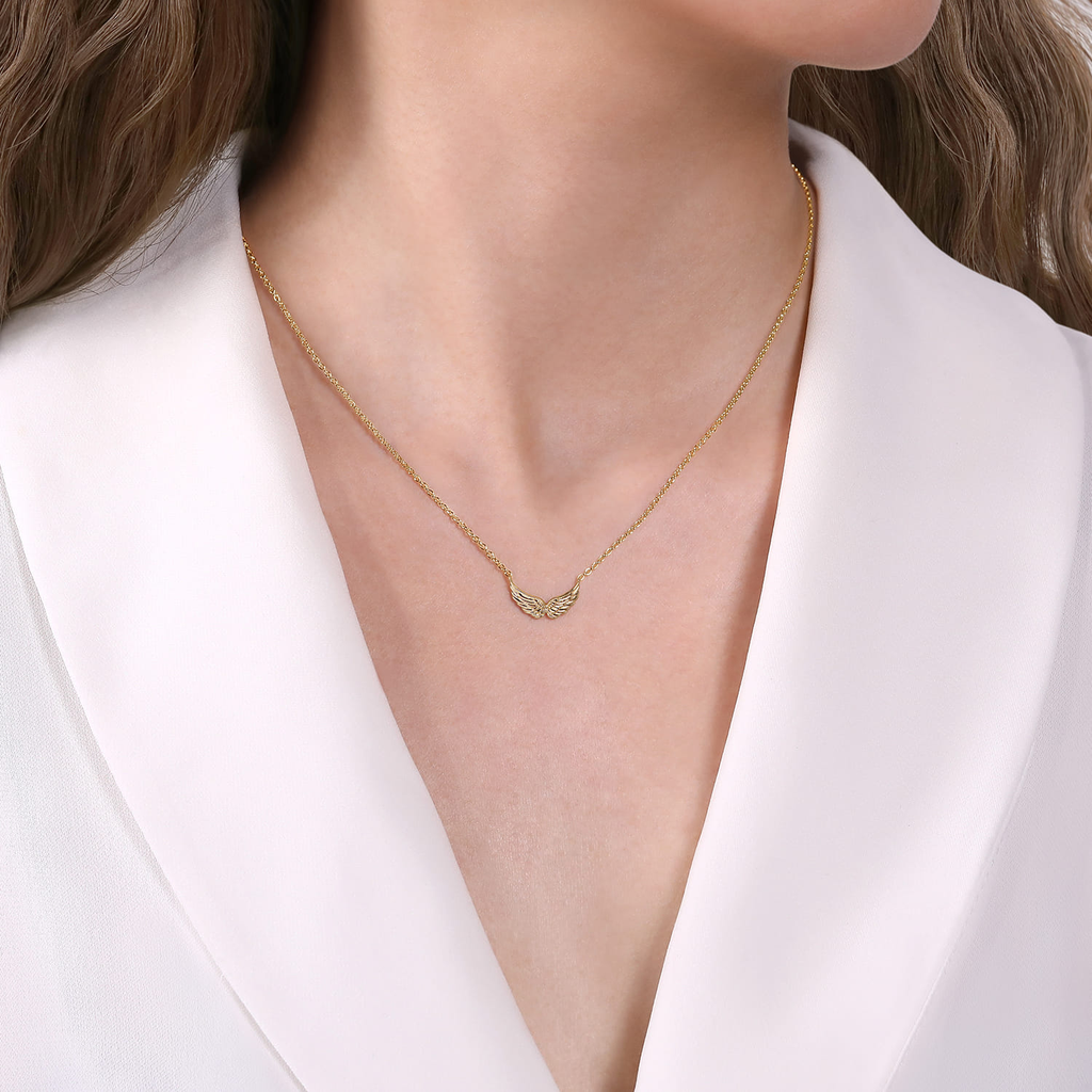 model wearing gold necklace with angel wings in the center on natural background