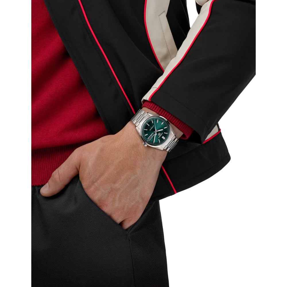 Person wearing a steel TAG Heuer watch with a green dial on a white background