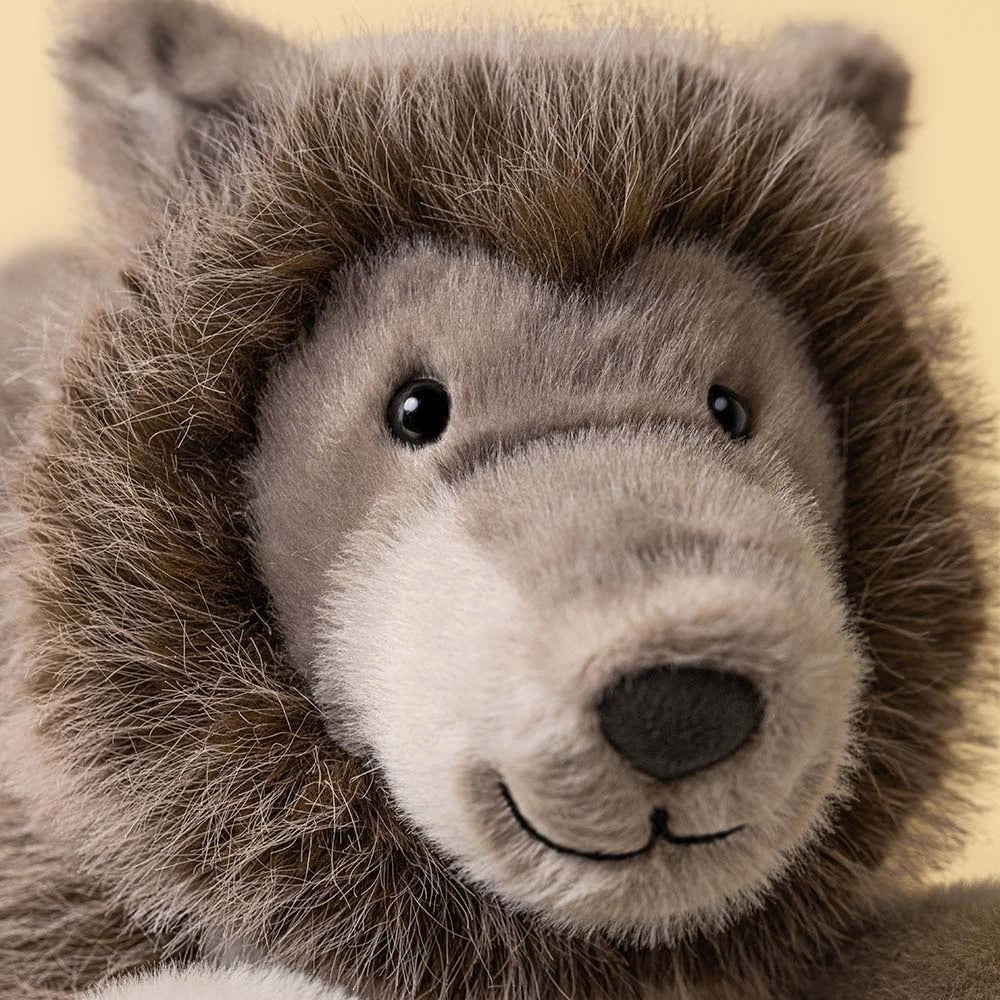 Close-up of a plush stuffed animal head with brown and gray fur, black eyes, and a stitched smile on a pale yellow background.