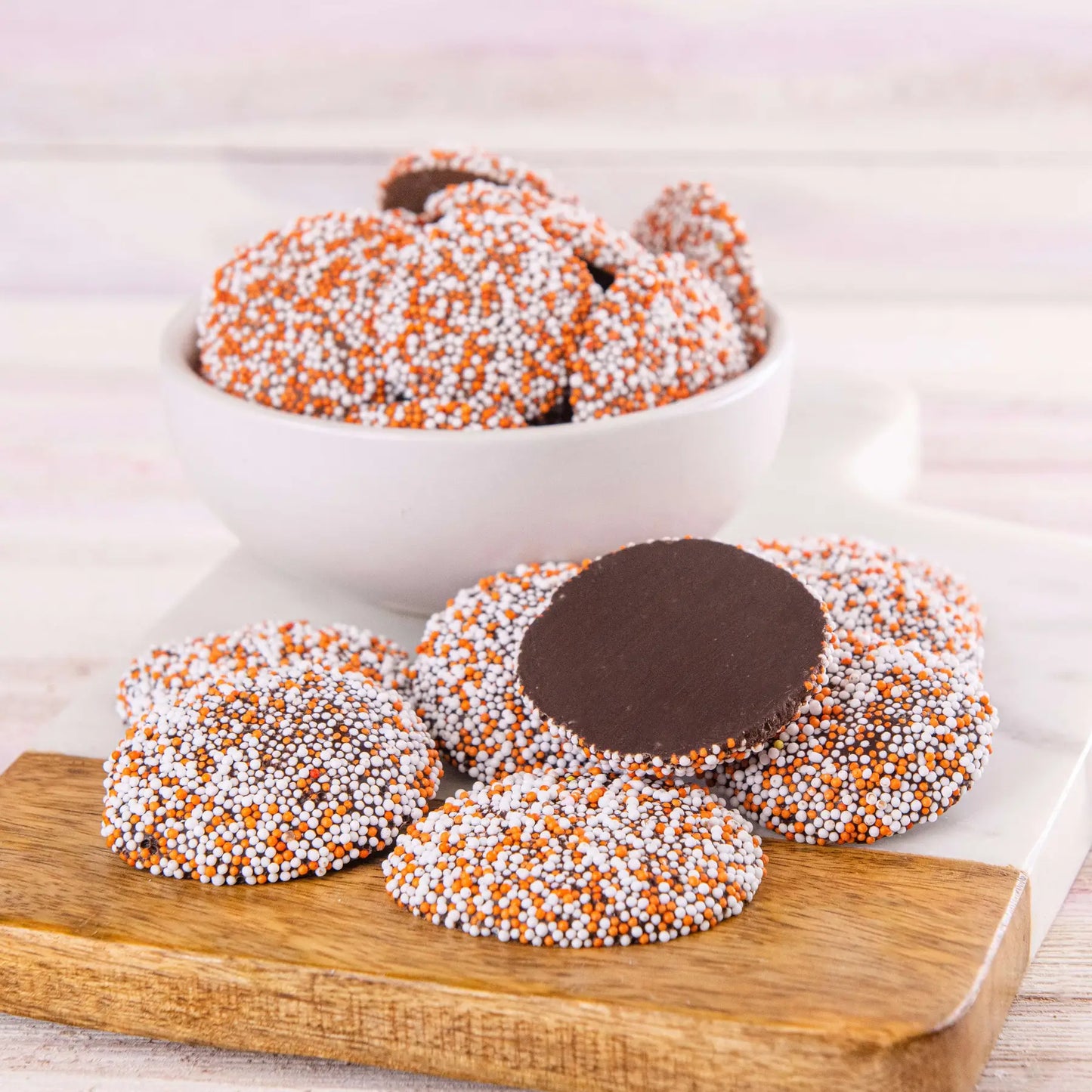  Chocolate topping and orange and white sprinkles on a wooden board.