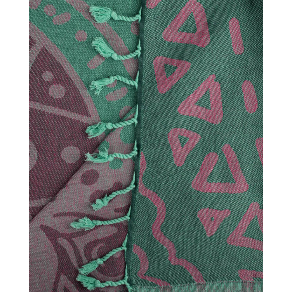 Close-up of a  beach towel with a turtle design in green, pink and brown with a green tassel edge on a white background.