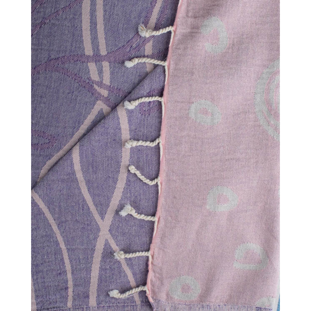 A close-up of a beach towel with a wave, shell,  and sea turtle pattern with a white tassel edge on a white background.