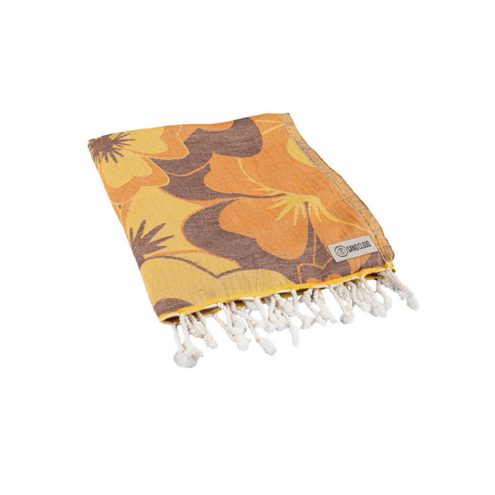 A folded floral patterned beach towel with orange and brown colors and a white tassel edge on a white background.