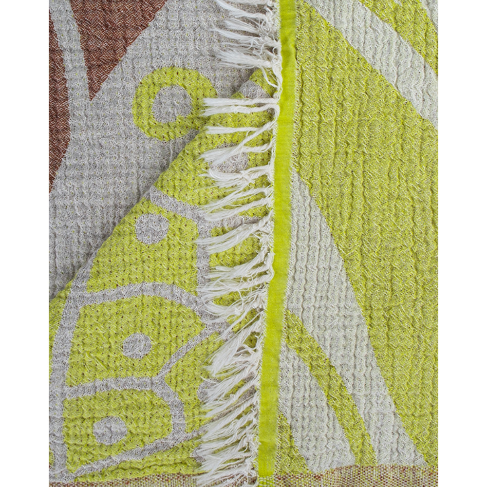 A close up photo of a beach towel with a yellow and brown sea turtle pattern and white tassel edge on a white background.