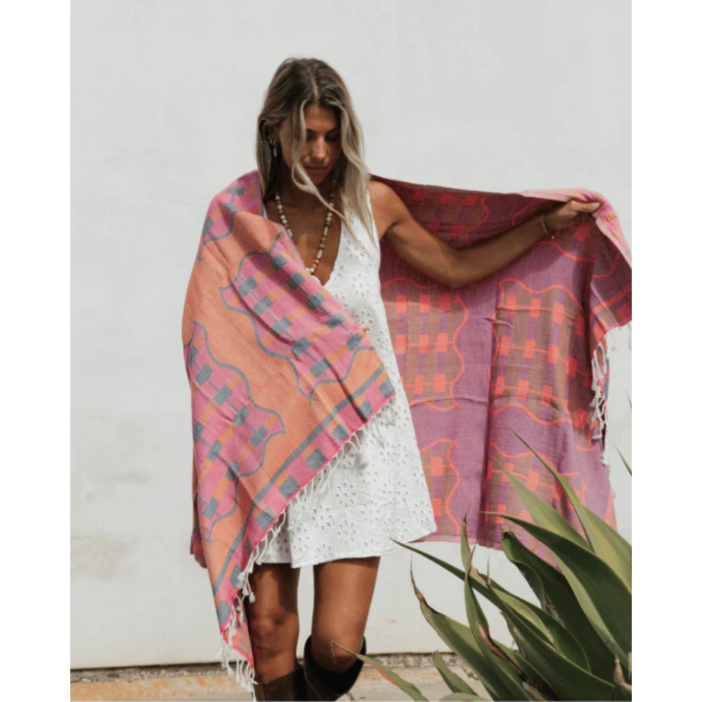 Woman holding a colorful patterned towel against a white wall.