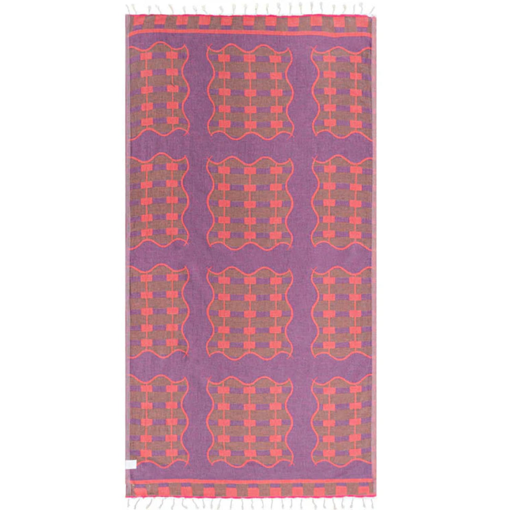 A photo of side two of a reversible patterned towel with a colorful  geometric design in orange on a purple base on a white backround.