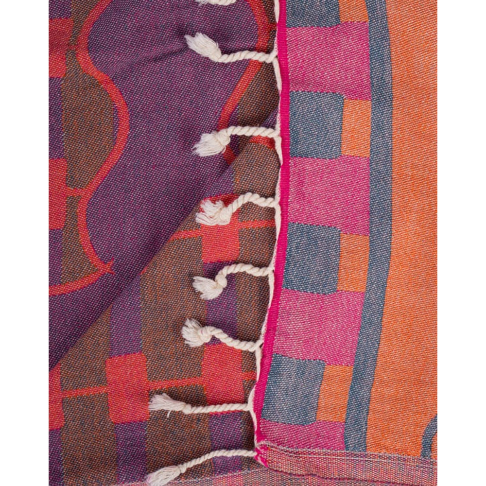 Close-up of a colorful woven textile with colorful geometric patterns and white fringe tassal ends on a white backround.