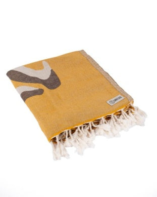 Folded yellow towel with fringe and abstract design on a white background.