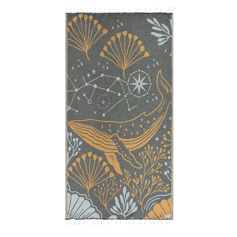 Side one of a colorful beach towel with a gold & blue highted whale and sea life pattern on a gray base color on a white backround. 