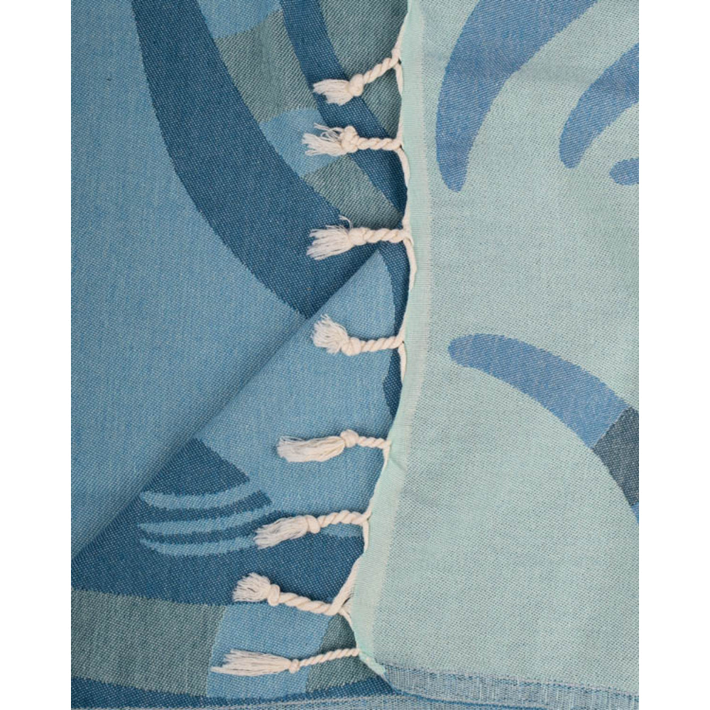 A close up photo of a blue beach towel with two reversible patterns with a seal design and blue wavy patterns on and a white fringe edge tassel on  white background.