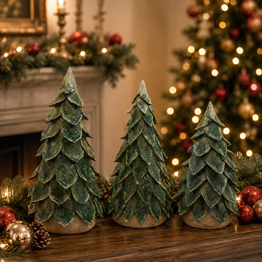 Three green pine tree holiday ornaments with textured, layered scales sit on a wooden mantel in a decorated living room with a Christmas tree and fireplace in the background.