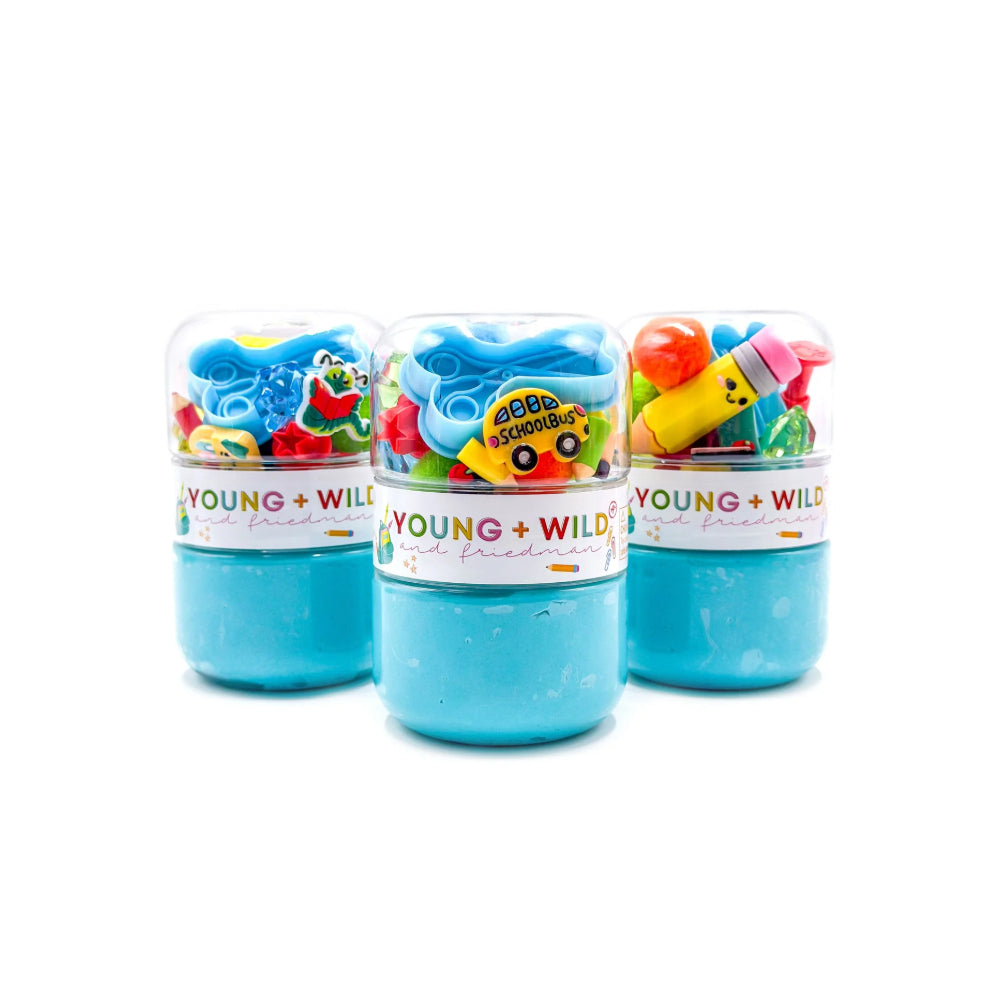 Three clear plastic jars filled with bright blue slime and colorful small accessories, arranged on a white background. The jars have white labels reading 'YOUNG + WILD' and are filled with blue slime.