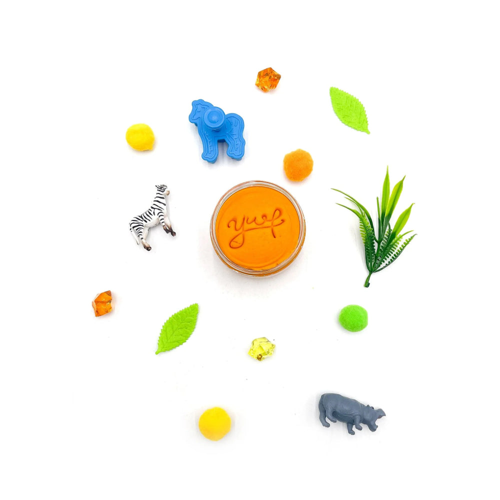 Aerial shot of an open jar of sensory dough stamped with the letters "YWF" with animal-shaped toys and leaves on a white background