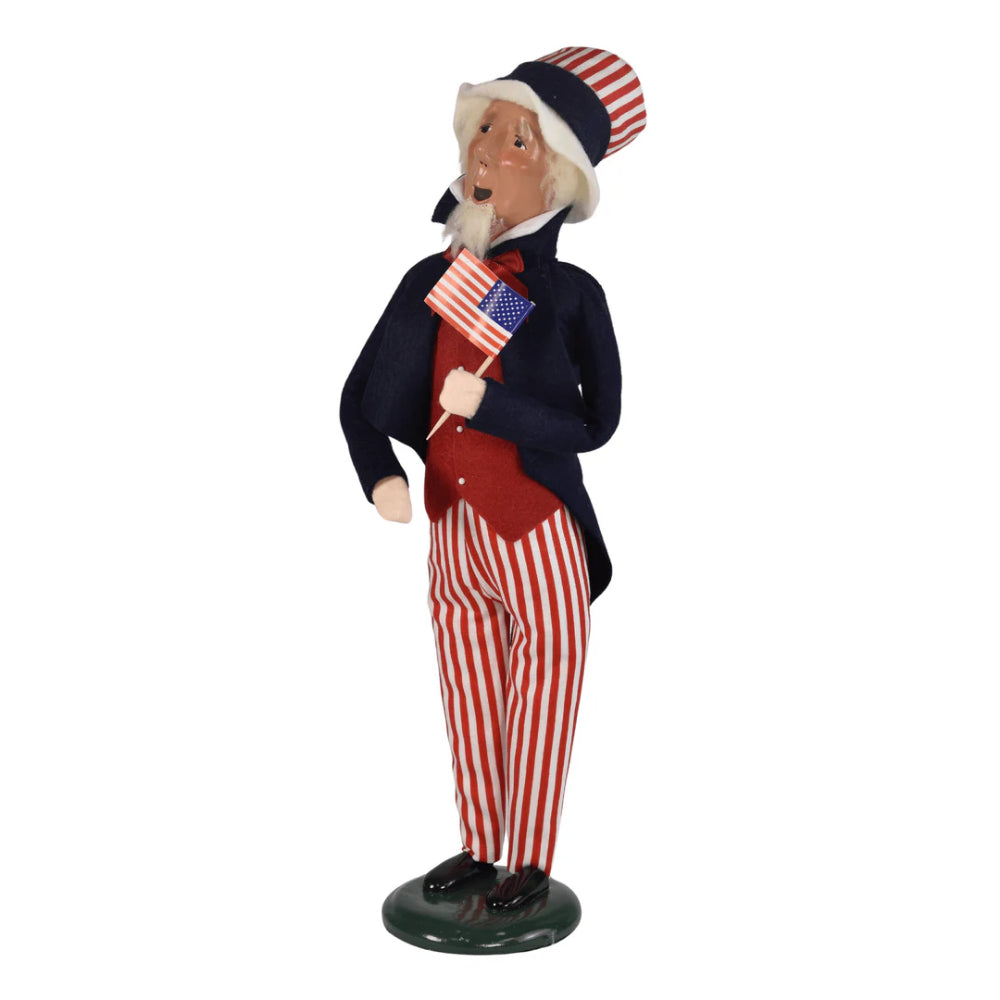 A right angled side photo of a figurine of  a caroling Uncle Sam holding an American flag on a white background