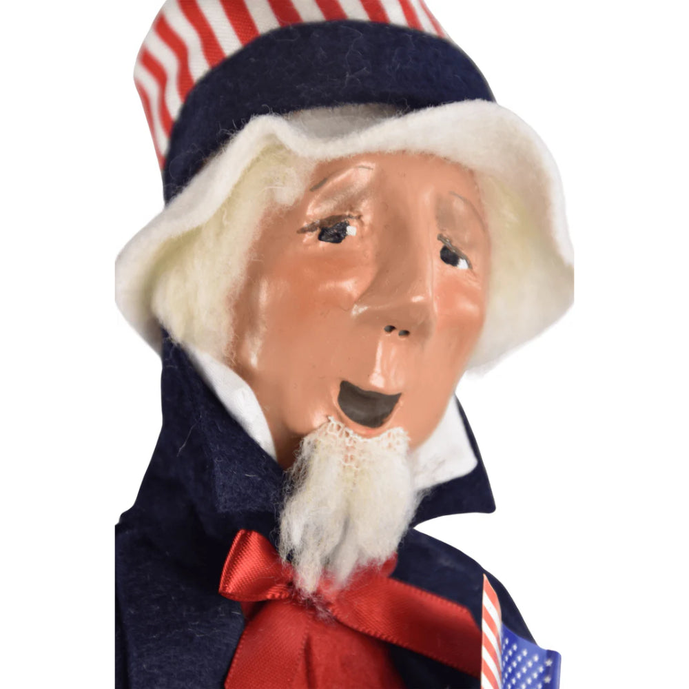 A close up photo of the face of a figurine of a caroling Uncle Sam holding an American flag on a white background