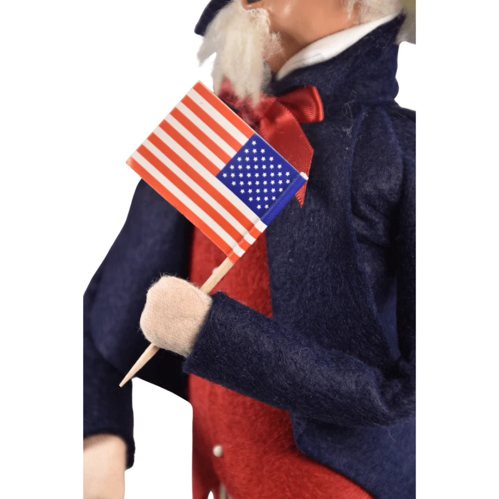 A close up photo the a American flag being held  by figurine of a caroling Uncle Sam holding an American flag on a white background