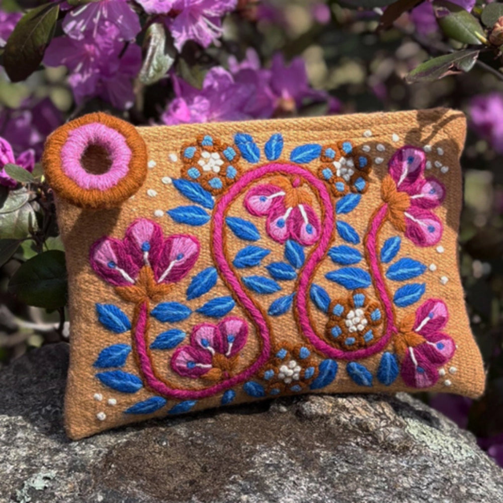 Decorative pouch with floral embroidery on a stone surface with purple flowers in the background
