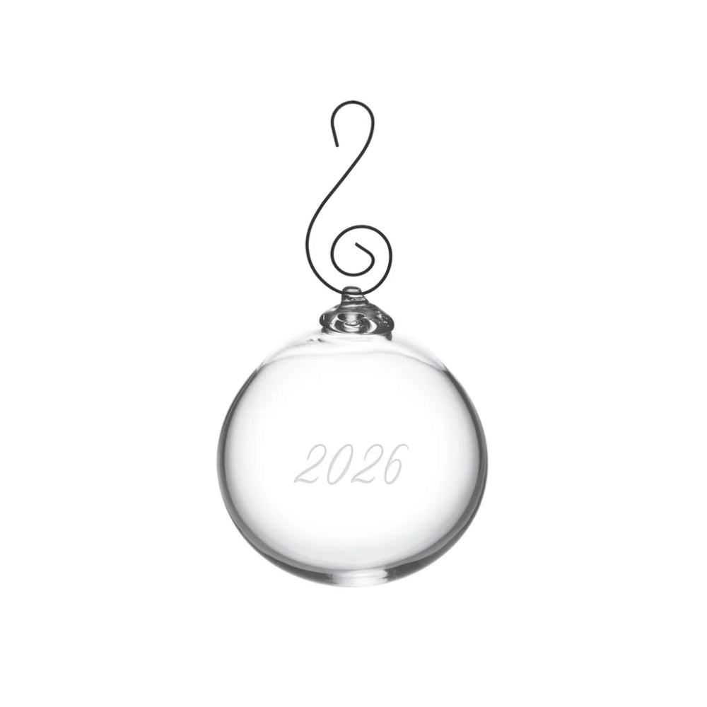 A clear glass Christmas ornament shaped like a round bauble with a black wire hanger and the year '2026' engraved on the front, shown on a plain white background.