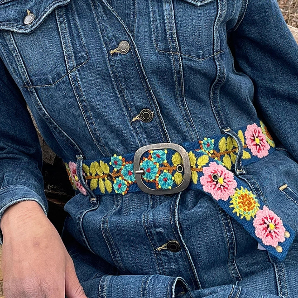 Person wearing a blue denim jacket with an embroidered floral belt.