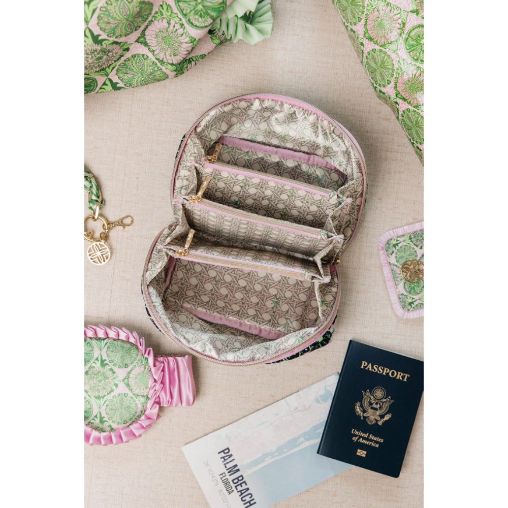 An open round zippered travel organizer pouch with multiple interior compartments, shown on a beige fabric surface with a passport, travel card, and matching patterned accessories around it.
