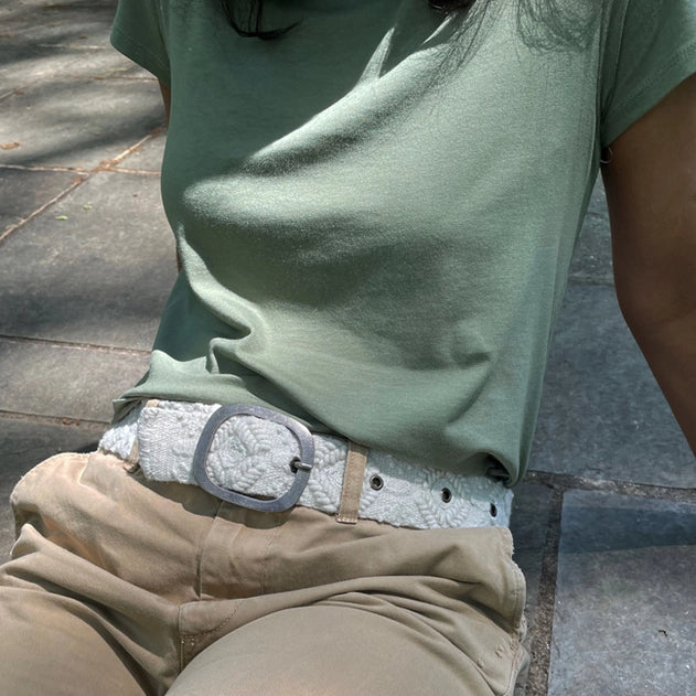 Person wearing a green t-shirt and beige pants with a textured belt, sitting on a stone surface.