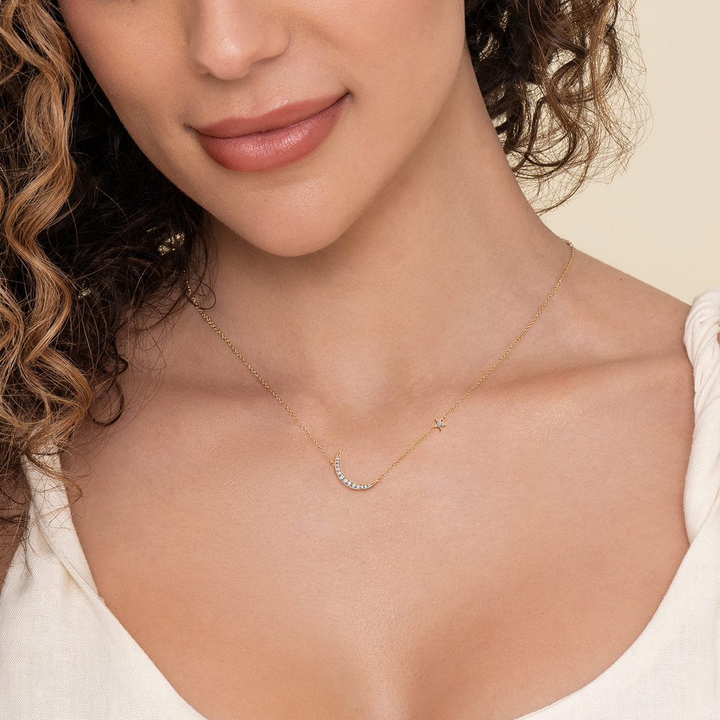 Close-up of a woman wearing a delicate gold necklace on a neutral background