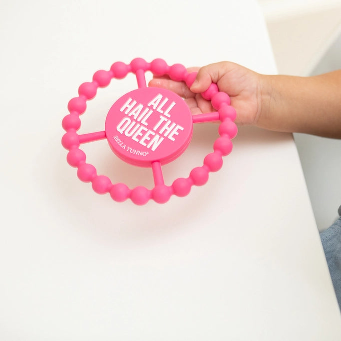 Pink beaded teether with 'All Hail The Queen' text held by a hand on a white background