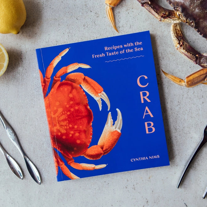 Cookbook titled 'CRAB' by Cynthia Nims on a table with crab ingredients.
