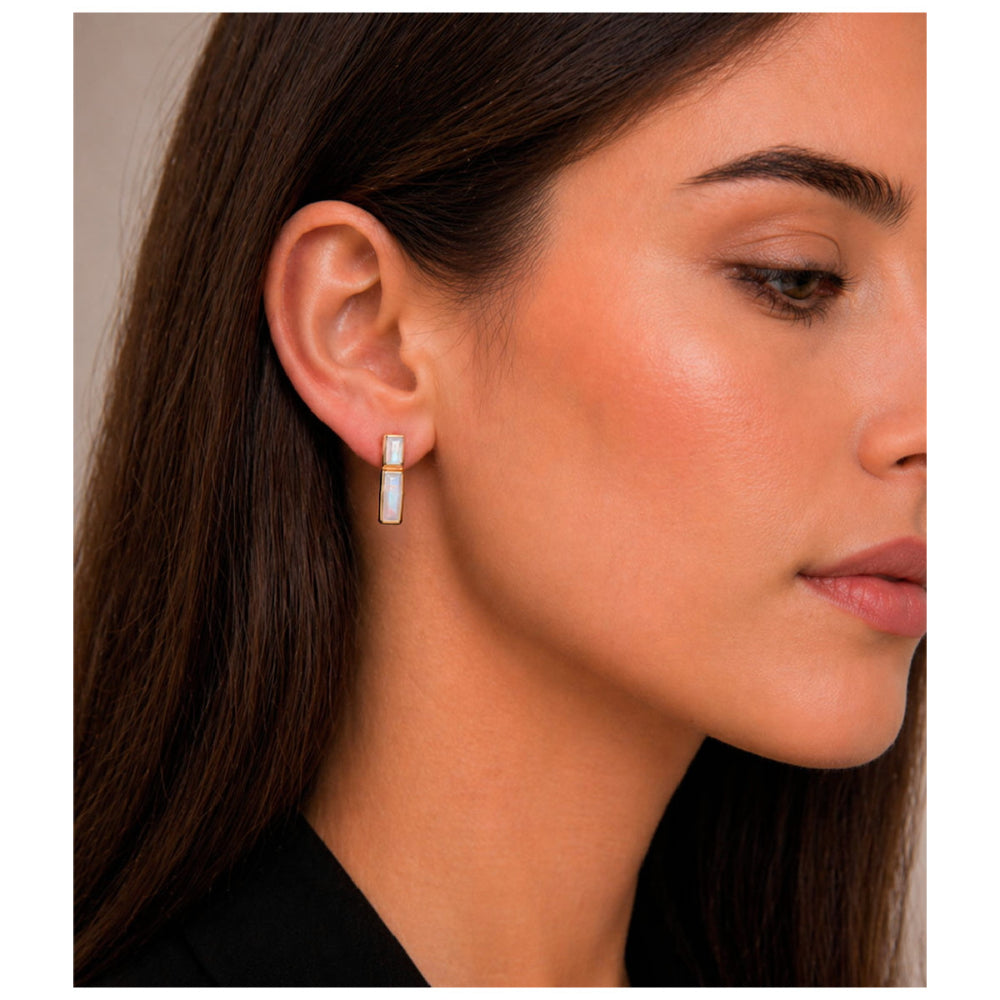 A close-up side profile of a woman wearing a small vertical bar earring with a white inlay on a silver-toned setting.